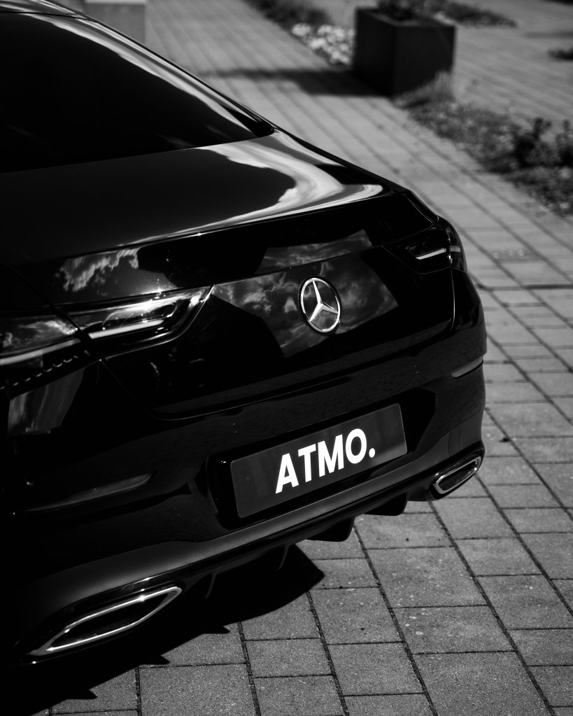 Black Mercedes car with a license plate reading 'ATMO.' parked on a brick pavement.