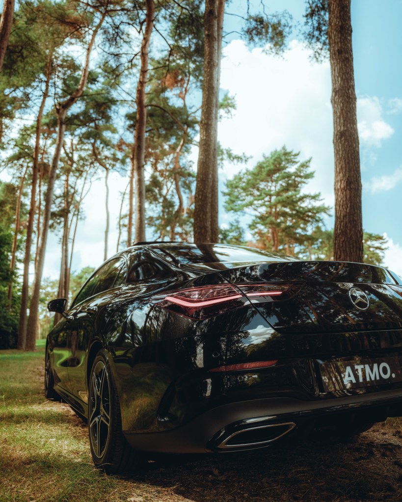 A black Mercedes-Benz car parked in a green forest, with tall trees and a clear sky in the background.