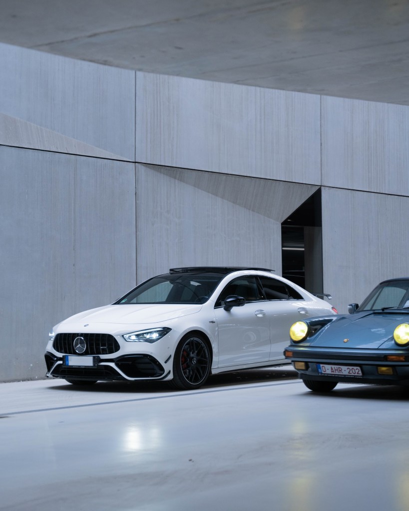 A modern white Mercedes-Benz car parked beside a vintage blue Porsche in a minimalist, industrial setting.