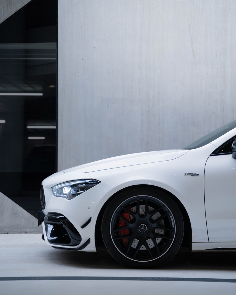 Close-up view of a white luxury car with a black wheel and red brake calipers, set against a sleek, modern background.