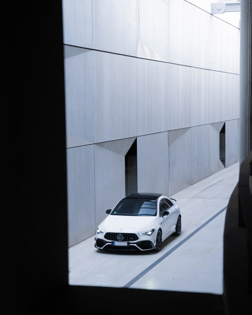 A modern white car parked in a sleek, contemporary corridor with gray walls and geometric designs.