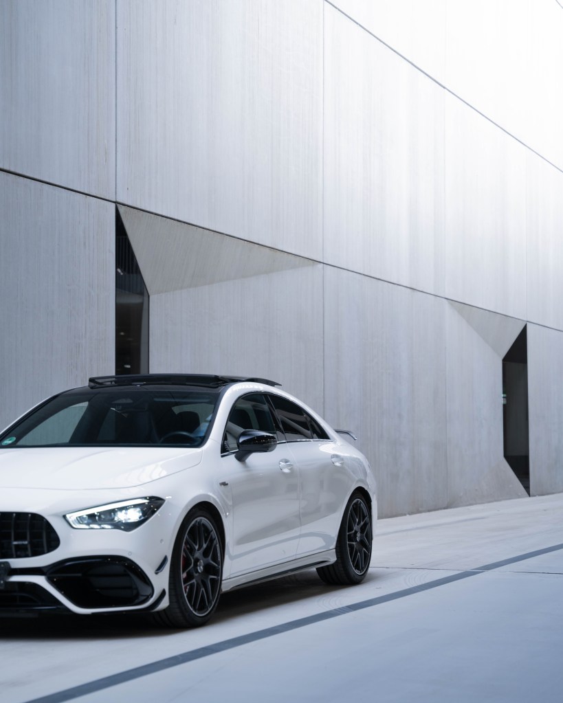 A sleek white sports car parked beside a modern concrete wall with geometric cutouts.